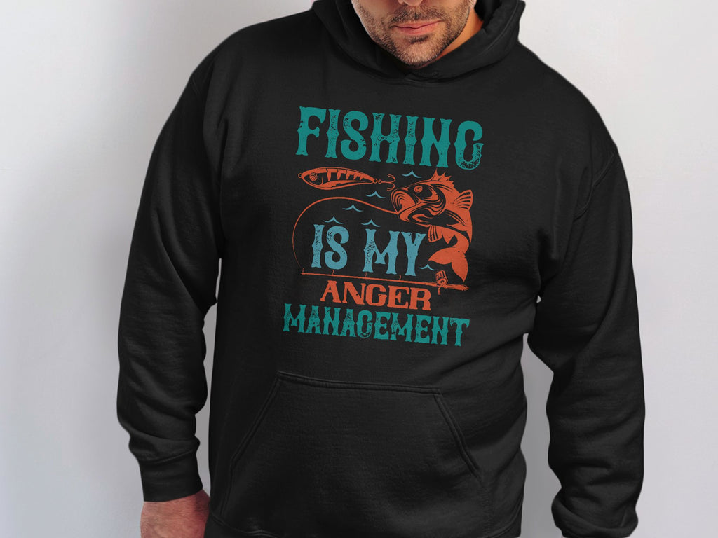 A person wearing a black hoodie from Garment Graphics featuring the text Fishing is my anger management in teal and orange. With a fish graphic, this Anglers Wardrobe piece is perfect for any fishing enthusiast.