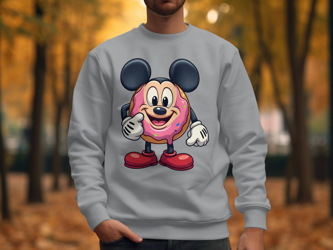 A quirky white T-shirt by Garment Graphics, featuring a cute cartoon mouse inside a donut, rests on a wooden surface. Nearby items for a playful wardrobe include a blue plaid shirt, headphones, a camera, and a white travel mug.