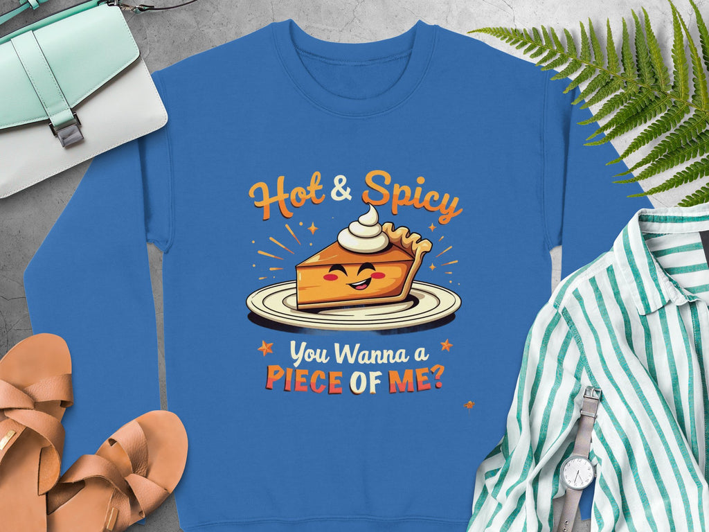 Garment Graphics offers a blue pie graphic sweatshirt with a smiling pie slice and whipped cream, featuring the text Hot & Spicy You Wanna a Piece of Me? This unisex piece is fun and quirky, perfect with sandals, a striped shirt, watch, purse, and green fern leaves.