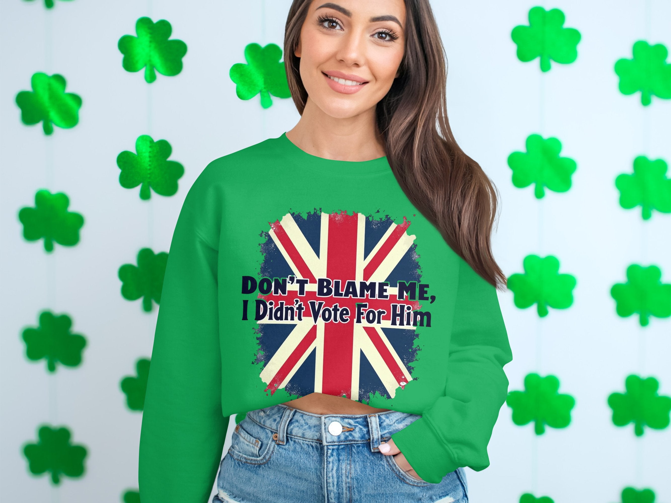 A person confidently models a green Garment Graphics sweatshirt featuring the Union Jack and bold text, Dont Blame Me, I Didnt Vote For Him, set against vibrant shamrocks. This stylish unisex piece ensures a perfect fit for all.