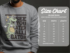 This Garment Graphics gray sweatshirt features a playful basketball-holding alligator and See You Later Alligator text. It comes in unisex sizes S to 5XL, with width and length measurements in inches shown on the Gildan 18000 size chart on the right.
