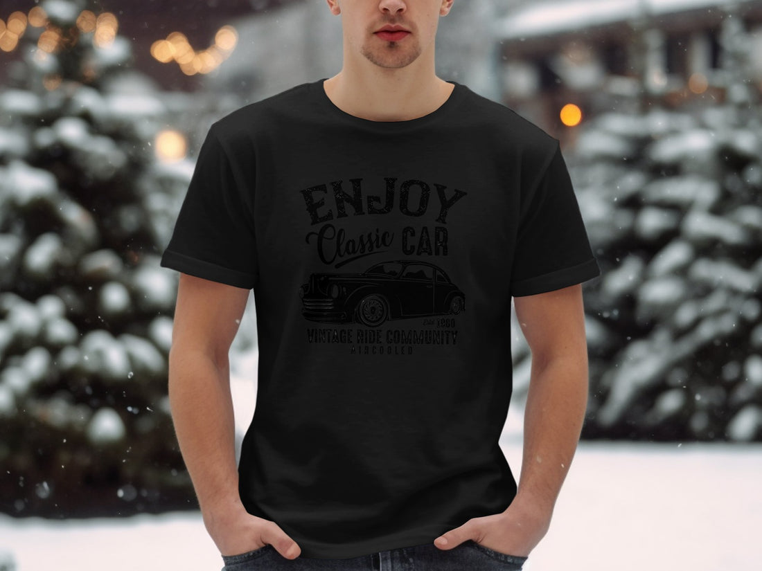 A person wears a white Garment Graphics T-shirt featuring a vintage car illustration and the text ENJOY Classic Car, Vintage Ride Community, Aircooled, estd 1980. Perfect for classic car fans, the scene shows a sandy beach with grass.