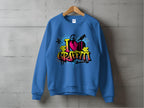 A Garment Graphics urban-style blue sweatshirt hangs on a wooden hanger against a gray wall, featuring an artistic graffiti design with I Love Graffiti in colorful letters and a silhouette of a spray-painting person.