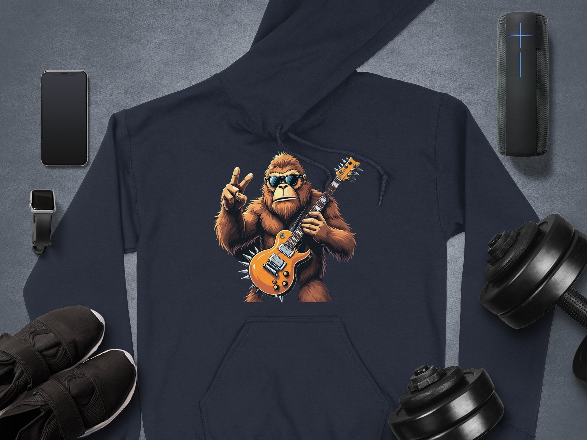 Discover Garment Graphics ultimate hoodie for music and animal lovers, featuring a gorilla graphic playing electric guitar with a peace sign. Its surrounded by essentials like a smartphone, smartwatch, wireless speaker, dumbbells, and black sneakers on a gray background.