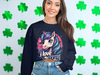 A woman wears a Garment Graphics sweatshirt with a colorful unicorn and I love my ponyunicorn text. She stands against a white wall with green clover decorations, highlighting the vibrant design.