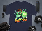 Garment Graphics navy T-shirt showcases a superhero graphic with a cartoon character emitting a green energy blast. Its Hero Time! bursts in bold orange and yellow letters. Surrounded by gadgets, sneakers, and dumbbells, its perfect for family sizing.