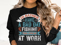 A person with long, wavy blonde hair is wearing a black unisex fishing sweatshirt by Garment Graphics. In bold, colorful letters, it reads: Id rather have a bad day fishing than a good day at work, highlighting their passion for fishing.