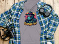 Garment Graphics grey hoodie boasts a gangster gorilla graphic with sunglasses, hat, and Gangster necklace. Crafted from medium-heavy fabric, its paired with a blue plaid shirt, headphones, a camera, and a white coffee cup lid on wood for a smokey cool vibe.