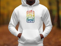 A person wears a retro graphic hoodie from Garment Graphics with Woodstock 1969 and illustrations of trees and a car against an earthy-toned, blurred outdoor backdrop.