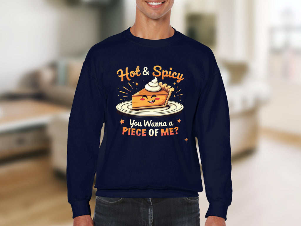 A person wears a navy blue unisex Garment Graphics sweatshirt featuring a pie graphic with whipped cream and stars. The text reads, Hot & Spicy. You Wanna a Piece of Me? against an indistinct indoor backdrop.