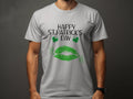 A person wears a Garment Graphics T-shirt featuring Happy St. Patricks Day and two green clovers on dark gray. Below, a bold green lip print embodies the festive spirit with its vivid design of lips and clovers.