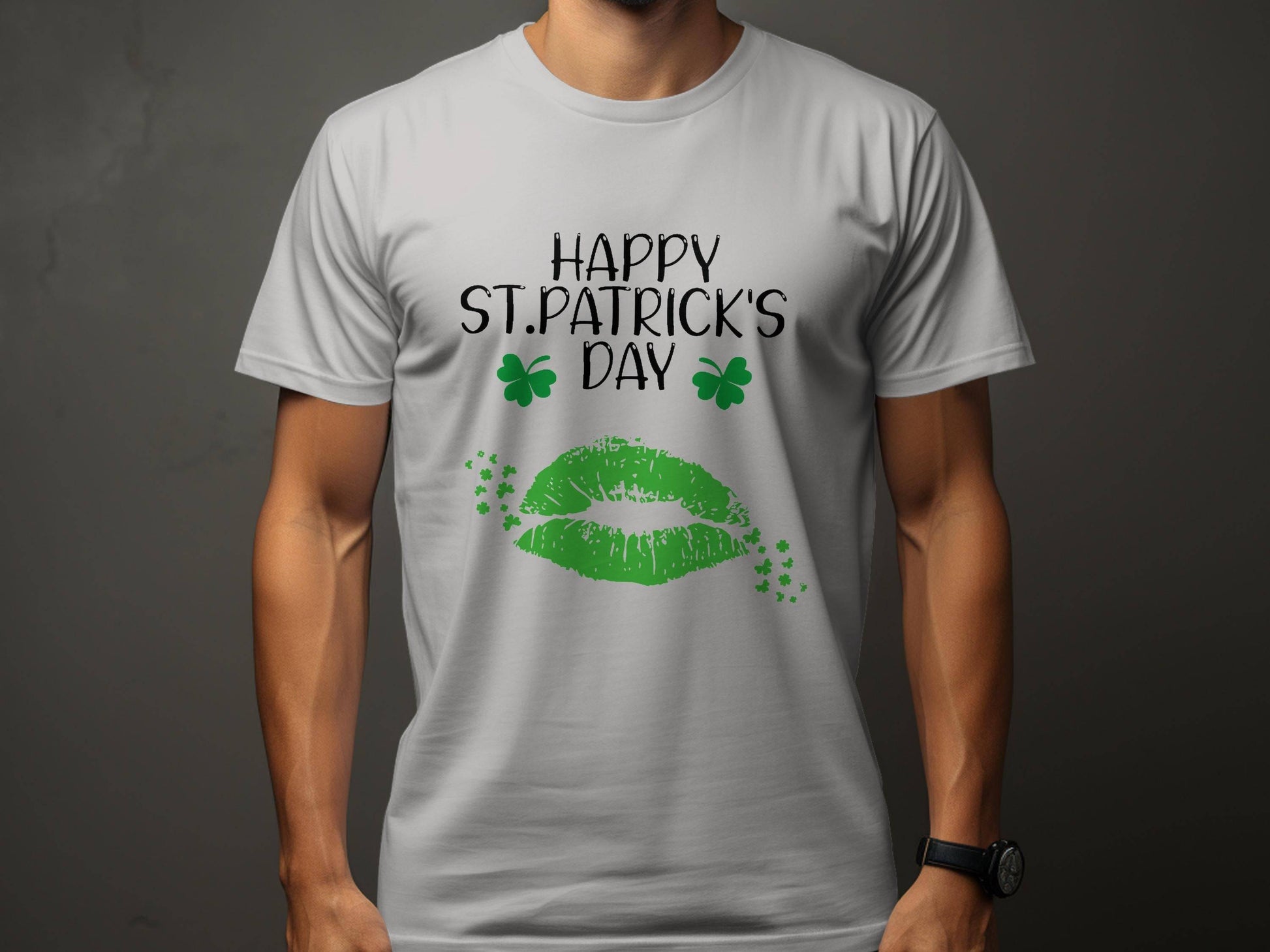 A person wears a Garment Graphics T-shirt featuring Happy St. Patricks Day and two green clovers on dark gray. Below, a bold green lip print embodies the festive spirit with its vivid design of lips and clovers.