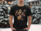 In a snowy scene, someone wears a Garment Graphics black T-shirt with a Bigfoot-like creature, sunglasses on, holding an electric guitar and giving a peace sign—ideal for music enthusiasts.