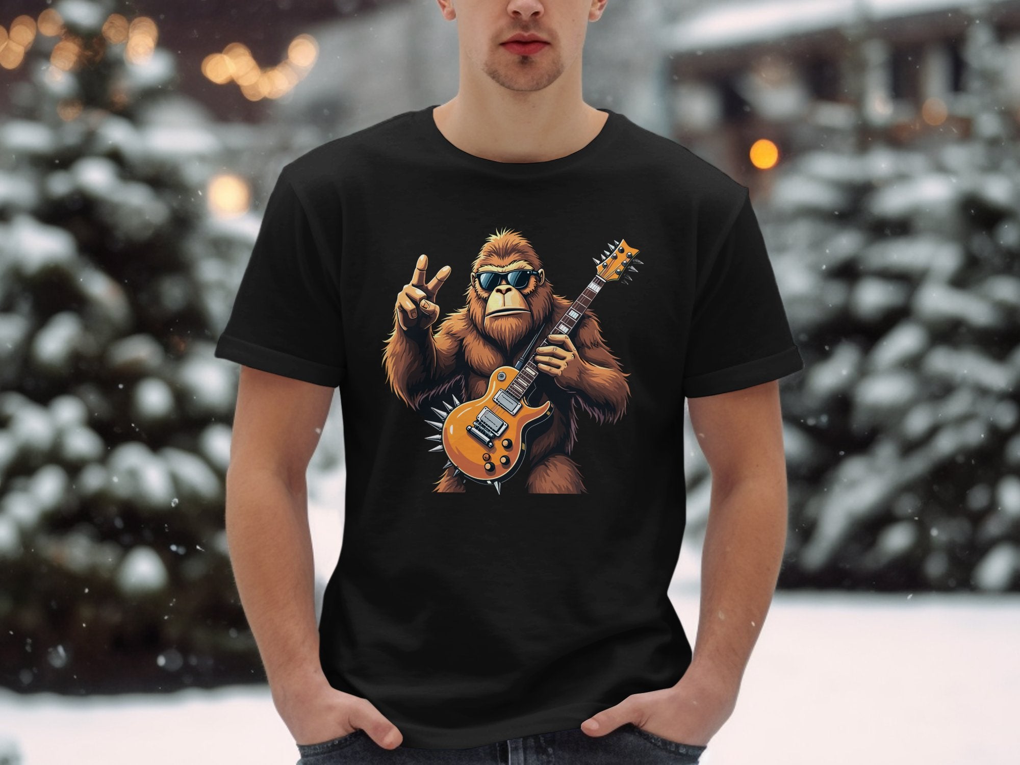 In a snowy scene, someone wears a Garment Graphics black T-shirt with a Bigfoot-like creature, sunglasses on, holding an electric guitar and giving a peace sign—ideal for music enthusiasts.