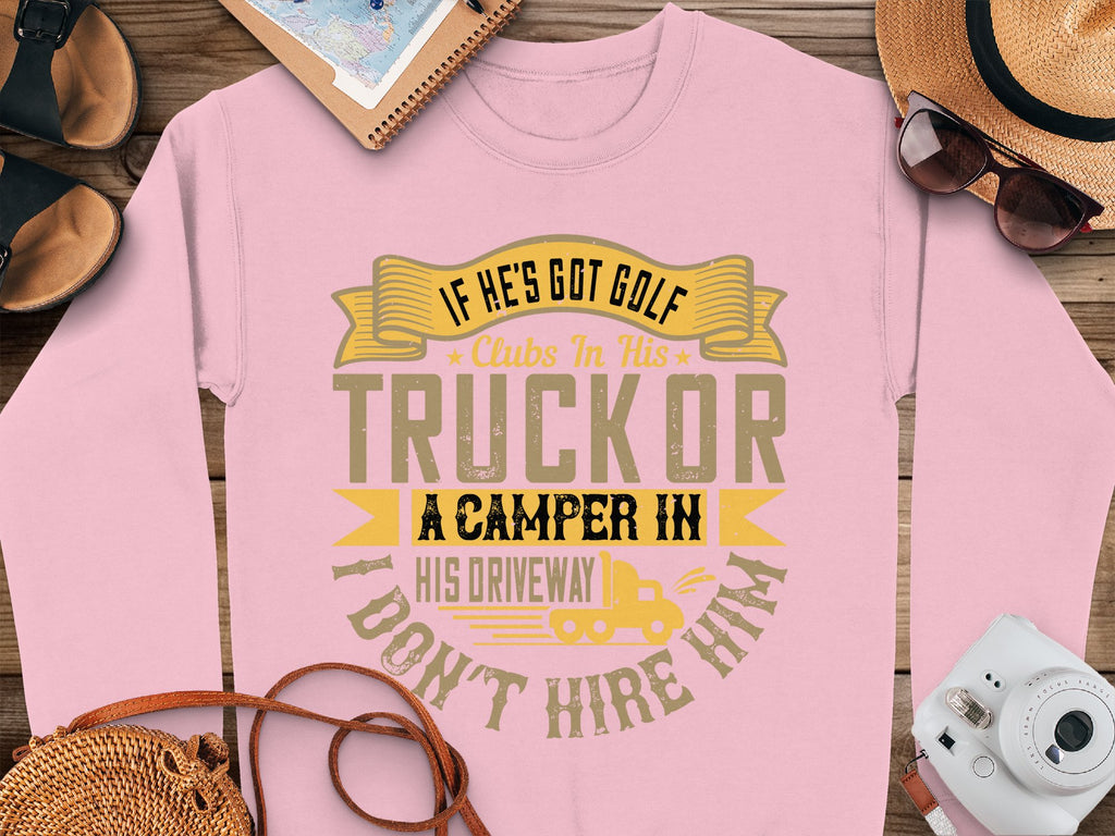 Garment Graphics humorous pink sweatshirt features the text: If hes got golf clubs in his truck or a camper in his driveway, dont hire him. Displayed with sunglasses, a notebook, straw hat, photo, and phone on a wooden surface—ideal for those who love casual wear with a witty twist.