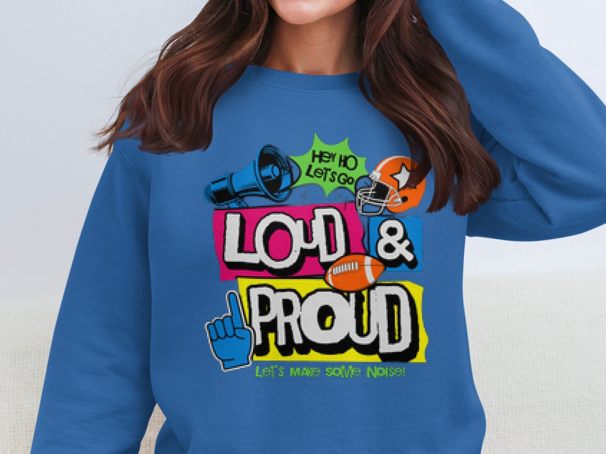 Someone sports a blue Garment Graphics sweatshirt boasting a megaphone, helmet, foam finger, and Loud & Proud with phrases like Hey Ho Lets Go. These unisex Loud and Proud Sweatshirts are perfect for making some noise!.