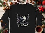 A black Garment Graphics shirt with an eagle spreading wings above Freebird, surrounded by pine branches, ornaments, pinecones, and a coffee cup on wood. This unisex piece merges comfort with bold style.