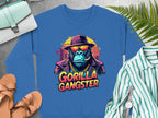 Garment Graphics presents a blue Gorilla Gangster sweatshirt featuring a gorilla in a hat, sunglasses, and gold chain, exuding urban style. Its surrounded by a striped shirt, brown sandals, purse, watch, and green ferns on a gray surface.