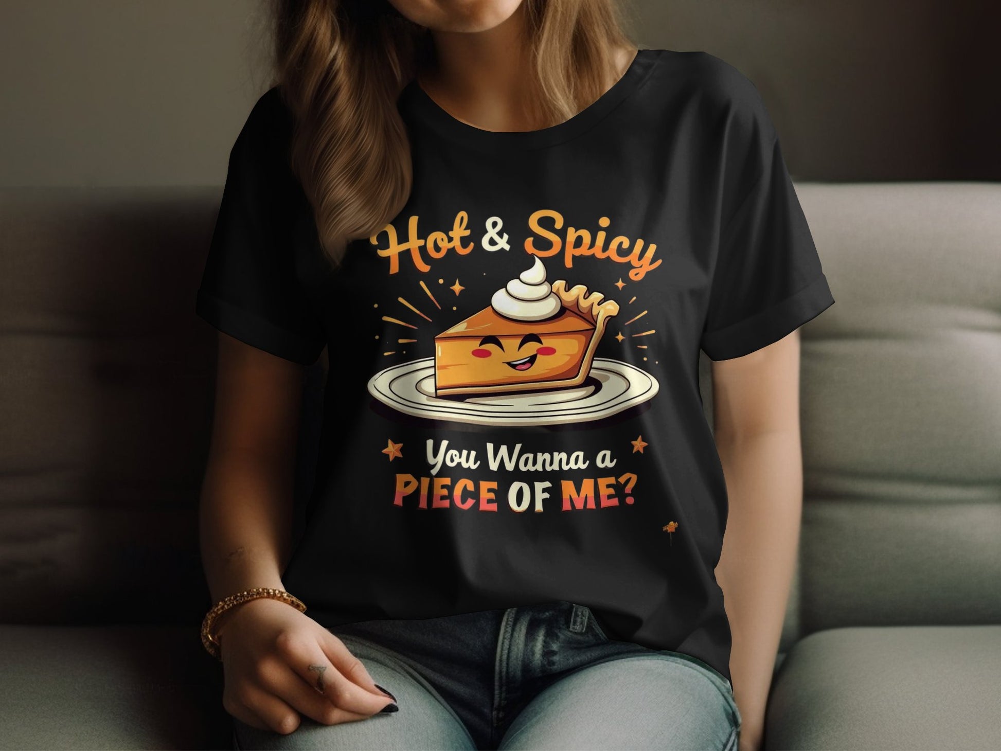 A person relaxes on a couch wearing Garment Graphics black T-shirt. The playful design features a cartoon pie slice with whipped cream and the text Hot & Spicy and You Wanna a Piece of Me? Perfect for casual outings, this stylish and cheeky top is available in womens sizing.