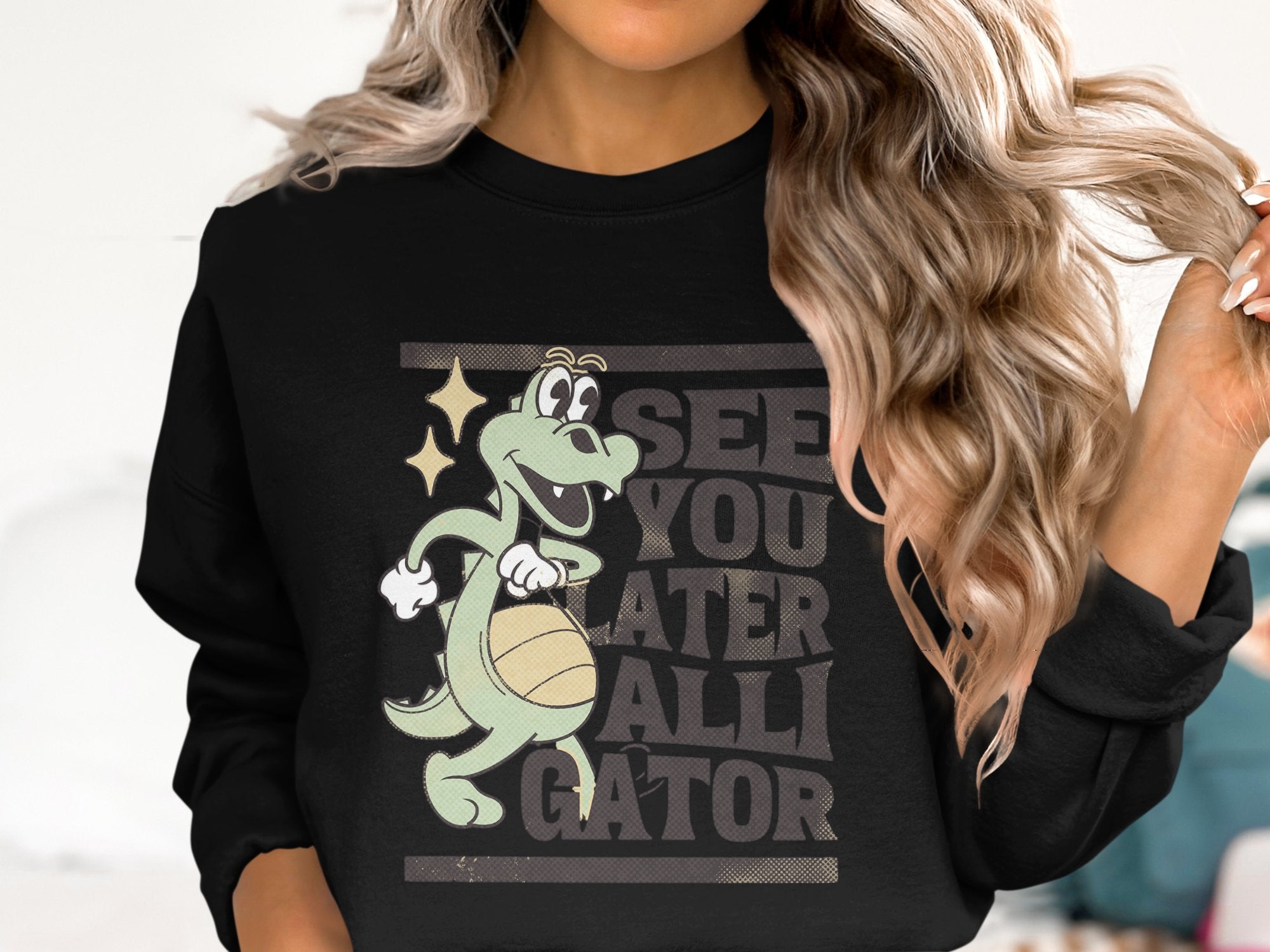 A person with long wavy hair sports a Garment Graphics sweatshirt featuring a cartoon alligator with a basketball and the words See You Later Alligator.