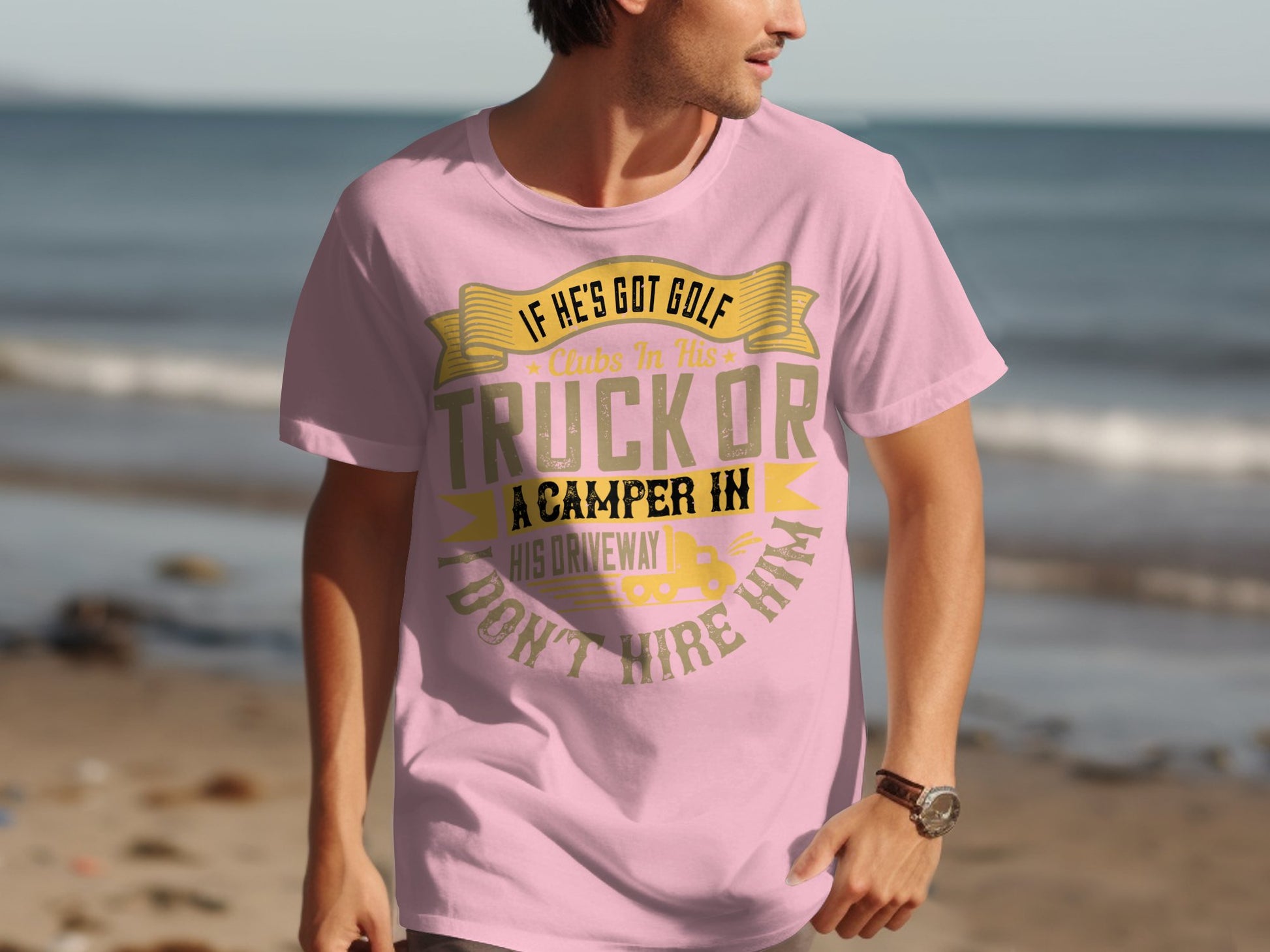 At the beach, a man sports a Garment Graphics pink t-shirt with the humorous quote: If hes got golf clubs in his truck or a camper in his driveway, I dont hire him, along with sand, ocean waves, and a clear sky—ideal for anyone who loves humor and the beach.