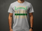 A Garment Graphics T-shirt showcases a witty design on white fabric, featuring the text If an Englishman gets run down by a truck, he apologizes to the truck in green and gold. The humorous shirt stands out against a neutral background, concealing the wearers face.