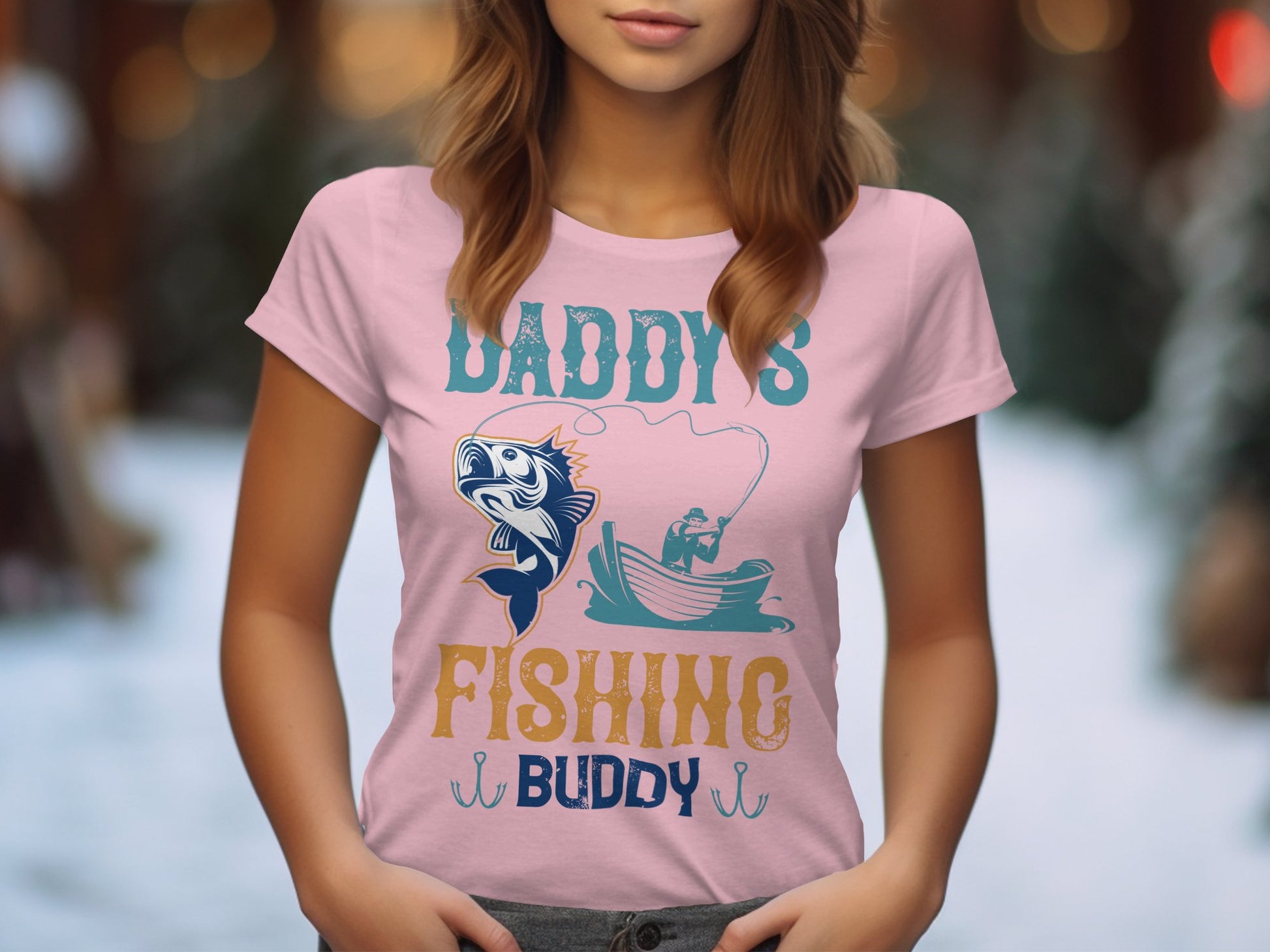 A woman wears Garment Graphics pink fishing t-shirt, reading Daddys Fishing Buddy, with a graphic of a fish and someone in a boat holding a fishing pole against hints of greenery and lights—a charming women’s fishing shirt.