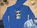 A Garment Graphics blue hoodie with a quirky llama in sunglasses and No Prob-Llama text, styled on wood with a plant, latte, and denim jacket for a cozy look.