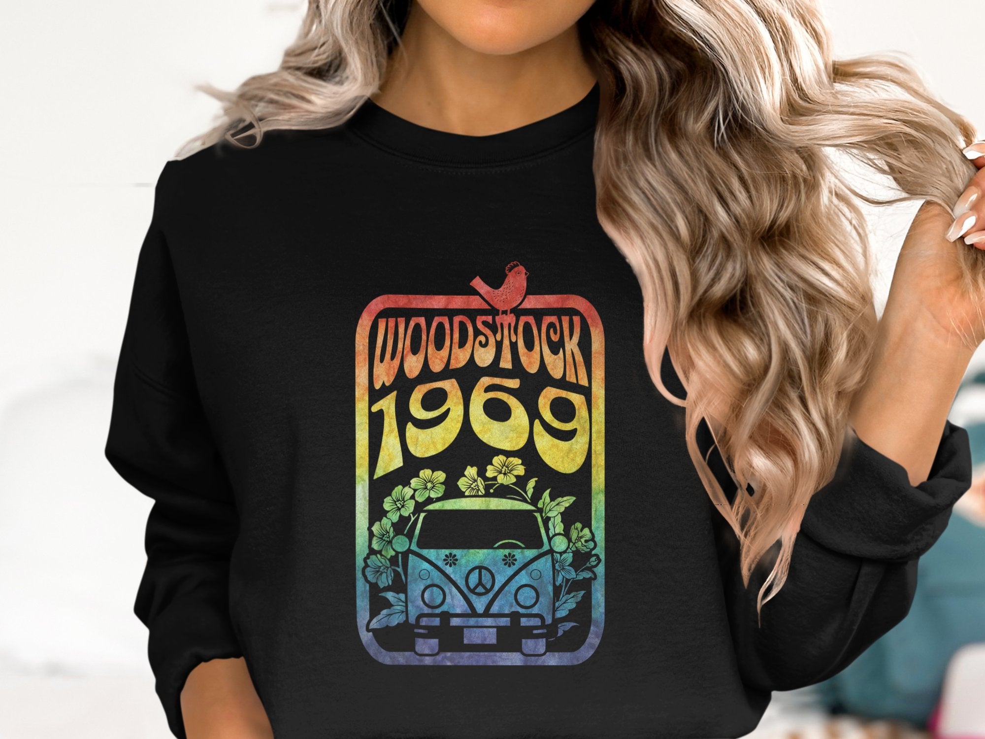Someone with long hair dons a retro-inspired black sweatshirt from Garment Graphics. The vibrant design showcases Woodstock 1969, a bird, flowers, and a van reminiscent of the famous Woodstock festival.