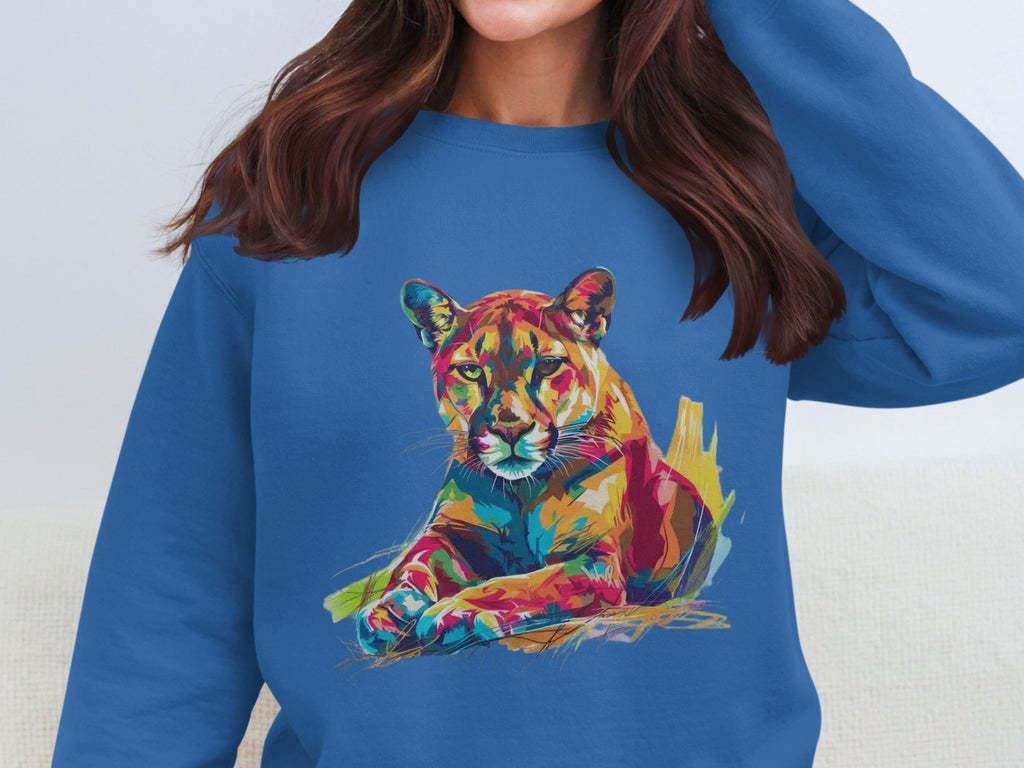 Someone in a blue sweatshirt from Garment Graphics, featuring a vibrant lounging cougar design, adjusts their hair with their face unseen.