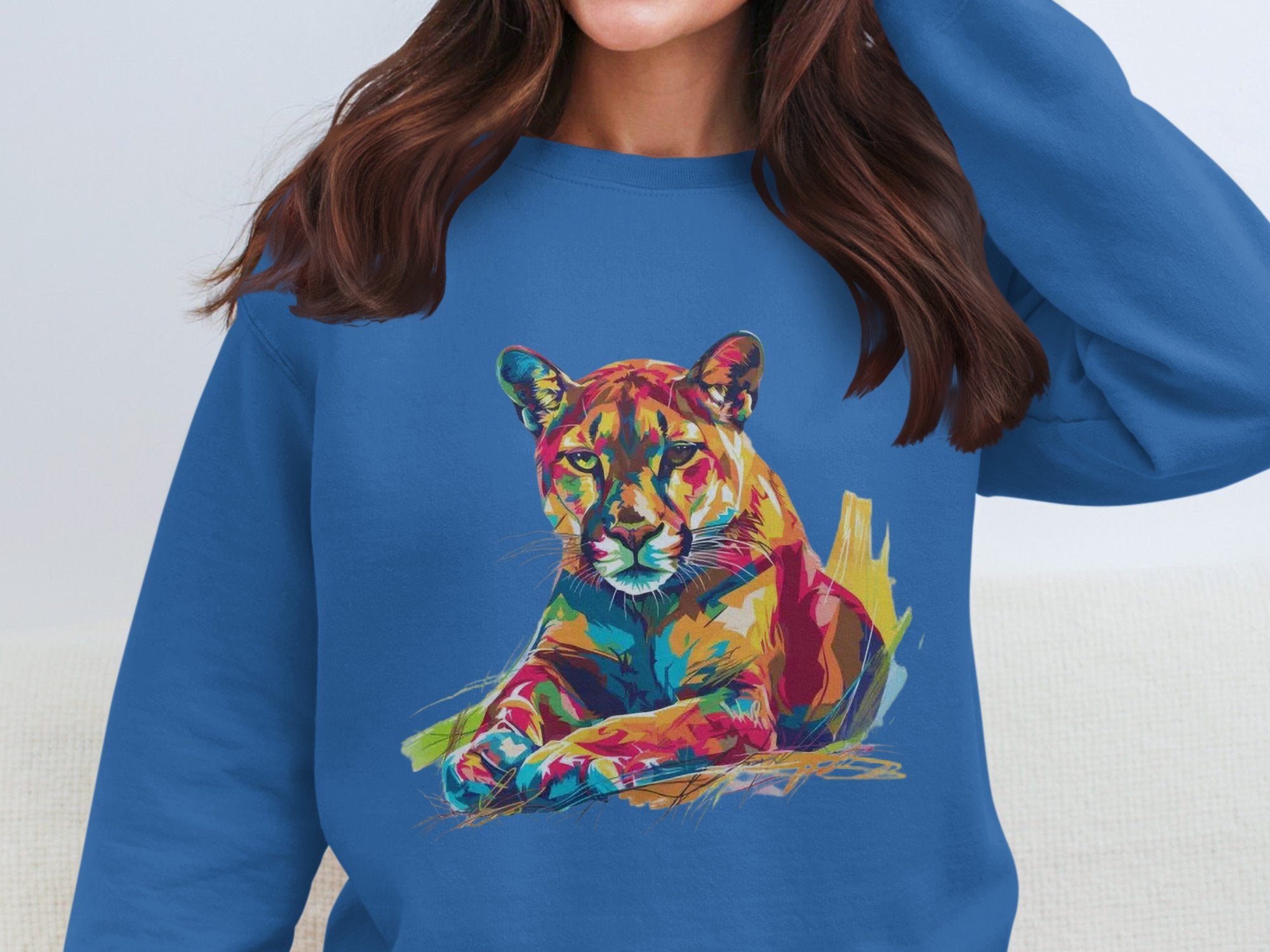 Someone in a blue sweatshirt from Garment Graphics, featuring a vibrant lounging cougar design, adjusts their hair with their face unseen.