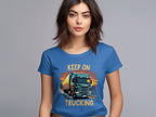A woman with brown hair, in a blue Keep on Trucking T-shirt by Garment Graphics featuring a bold truck graphic, stands against a gray background. Its ideal for trucking enthusiasts, embodying the spirit of the open road.