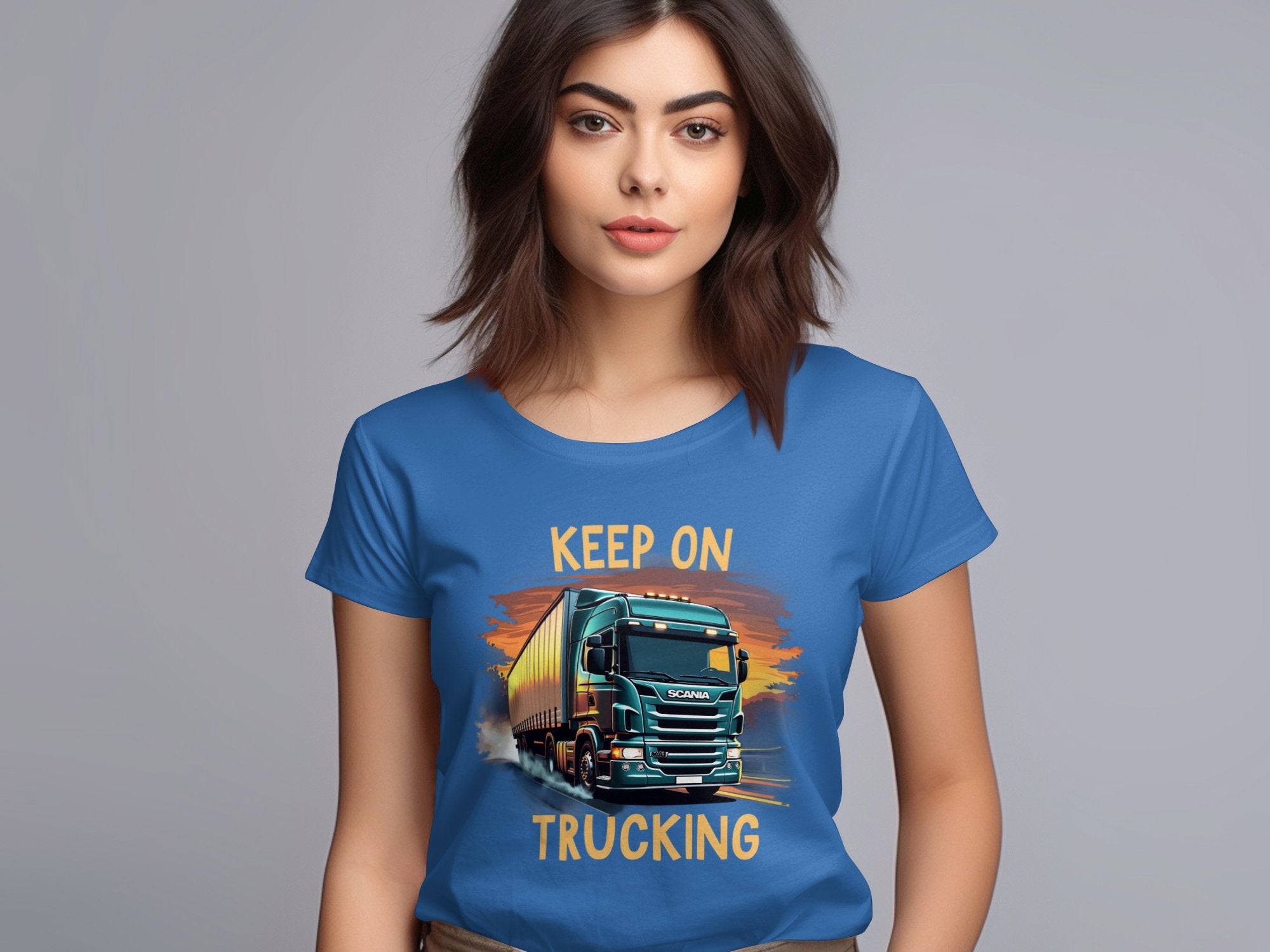 A woman with brown hair, in a blue Keep on Trucking T-shirt by Garment Graphics featuring a bold truck graphic, stands against a gray background. Its ideal for trucking enthusiasts, embodying the spirit of the open road.