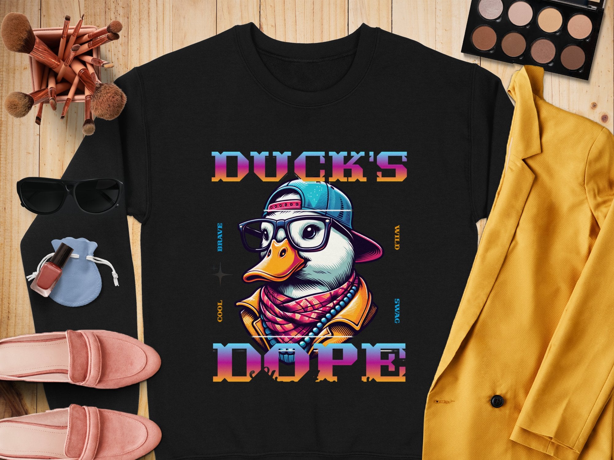 The Garment Graphics sweatshirt boasts a chic black design featuring a cartoon duck with glasses, hat, and scarf. It’s emblazoned with Ducks Dope in vivid letters, making it a bold fashion statement that pairs well with makeup brushes, sunglasses, pink shoes, and a mustard jacket.