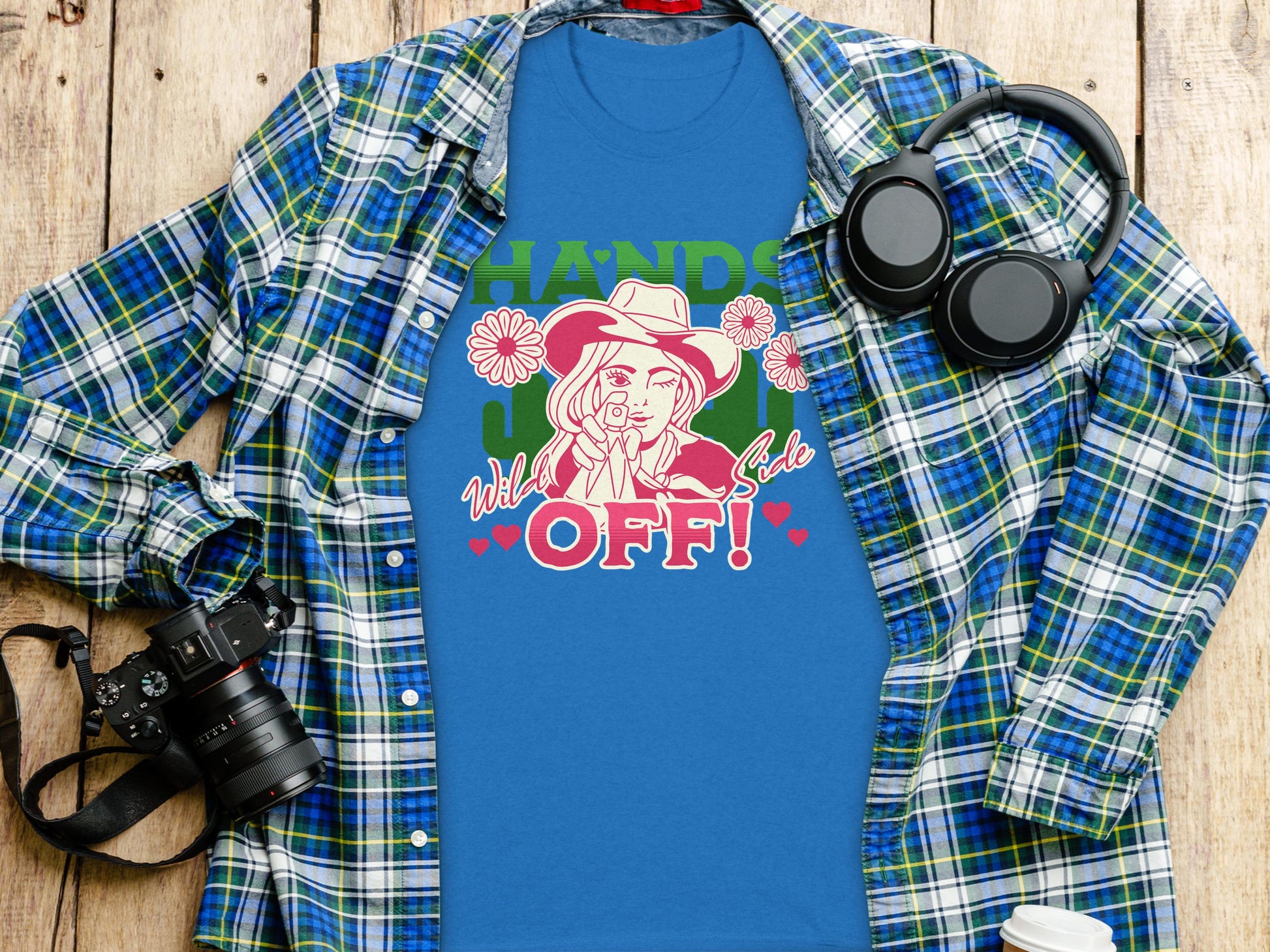 The classic fit blue t-shirt by Garment Graphics features a bold design of a dog in a cowboy hat with Hands off! Wild side text, styled on wood with a plaid shirt, camera, headphones, and water bottle—ideal for adventure lovers.