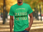 A person wearing a Garment Graphics green t-shirt with a witty design saying, If an Englishman gets run down by a truck, he apologizes to the truck, stands against a blurred park backdrop with trees and autumn leaves.
