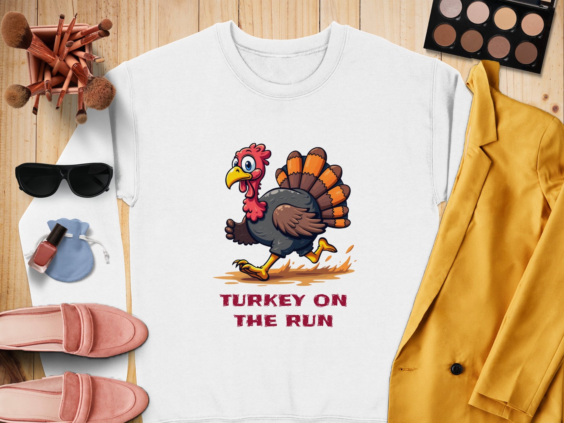 Flat lay showcasing a Garment Graphics white sweatshirt with a cartoon turkey and Turkey on the Run design. Accompanied by a yellow blazer, pink shoes, sunglasses, makeup brushes, eyeshadow palette, nail polish, and a blue pouch.