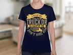 A person wears a Garment Graphics navy blue T-shirt featuring a humorous golf graphic with yellow text: If hes got golf clubs in his truck or a camper in his driveway, I dont hire him, making it pop against the blurred room background.