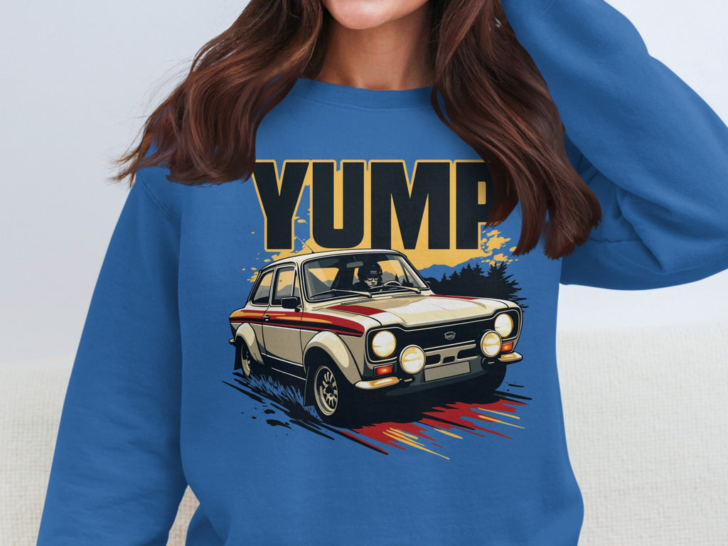 A woman wears a blue sweatshirt by Garment Graphics, boasting a vibrant rally car graphic with YUMP boldly displayed above. The classic car, featuring a red stripe, races through a dynamic, colorful backdrop, highlighting the iconic YUMP design.