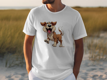 A dog lover wearing a Garment Graphics white T-shirt with a cartoon brown and white dog, expressing joy with a wagging tail, enjoys the sandy beach. A grassy field extends to the shoreline in the background.