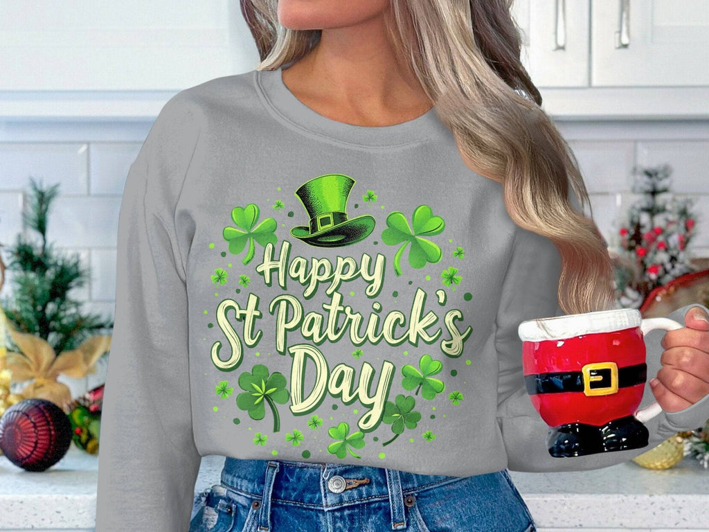 Amid festive cheer, someone holds a Santa-themed mug. Theyre in a Garment Graphics gray sweatshirt with shamrock graphics and green clovers, topped by a leprechaun hat proclaiming Happy St Patricks Day, surrounded by lively holiday decor.