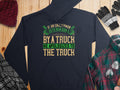 A Garment Graphics hoodie with the witty quote If an Englishman gets run over by a truck, he apologizes to the truck is displayed on a wooden surface, surrounded by a hat, gloves, flannel shirt, and other cozy clothing items.