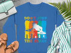 Garment Graphics blue sweatshirt features a vibrant DJ design with Dont Stop the Music text, ideal for music lovers. It pairs beautifully with a striped shirt, sandals, fern leaves, and a light blue purse to complete the look.
