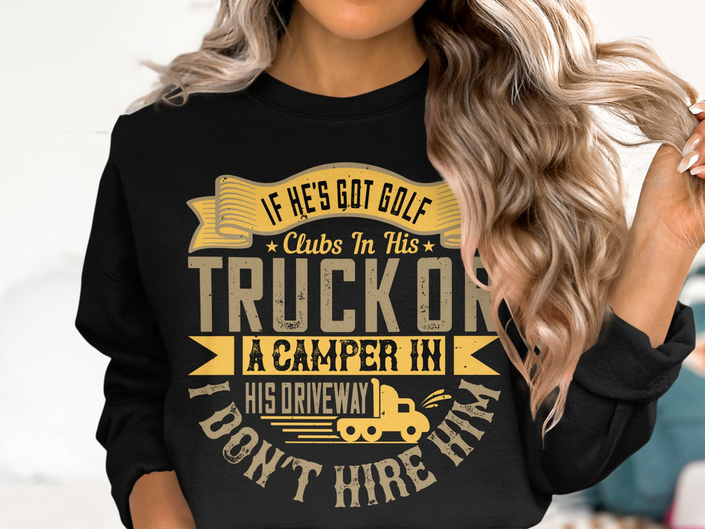A woman wears a black Garment Graphics sweatshirt with the humorous text: If he’s got golf clubs in his truck or a camper in his driveway, I don’t hire him, and graphics including a small truck. With long, wavy hair, she gently touches it with her left hand.