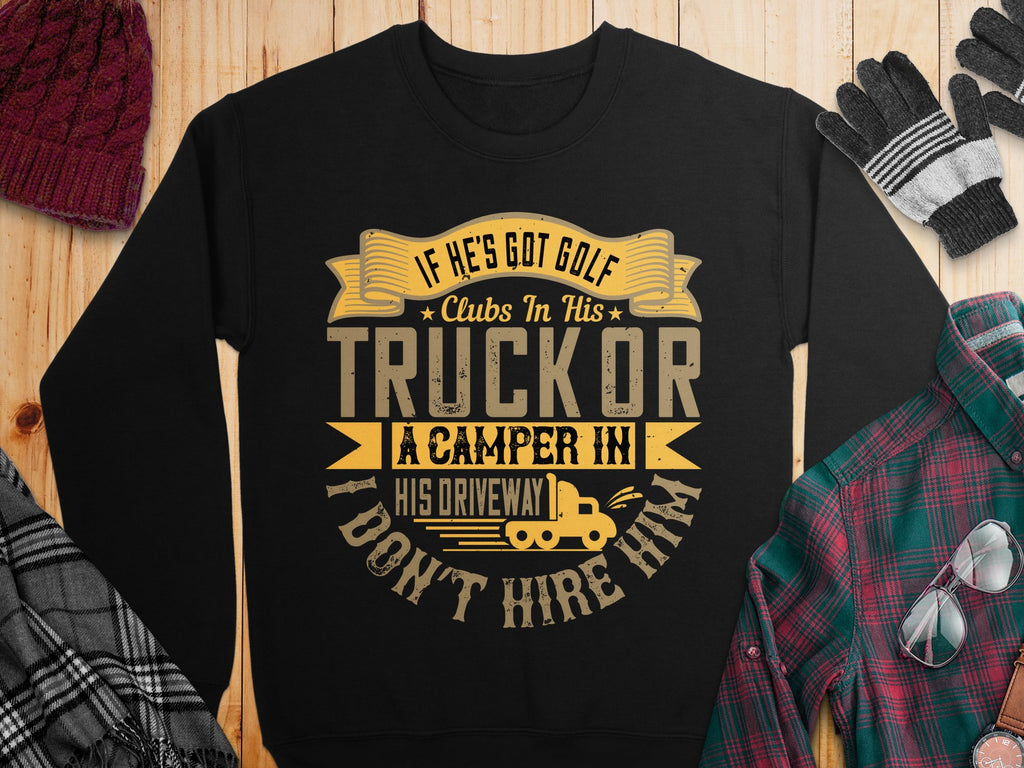 This black humorous sweatshirt by Garment Graphics features a yellow print saying, If hes got golf clubs in his truck or a camper in his driveway, I dont hire him. Laid on a wooden surface with a hat, gloves, and flannel shirt, its ideal for casual wear with a playful twist.