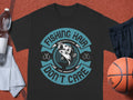 This black graphic tee from Garment Graphics showcases a one-of-a-kind fish design with teal text that reads Fishing Hair Dont Care. Styled on a sports theme, its paired with a basketball, water bottle, and gym shorts for an athletic look.