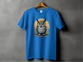 A Garment Graphics blue T-shirt showcases an owl with large, detailed eyes and feathers, set against an orange circle with plant motifs. The artistic design hangs gracefully on a wooden hanger.