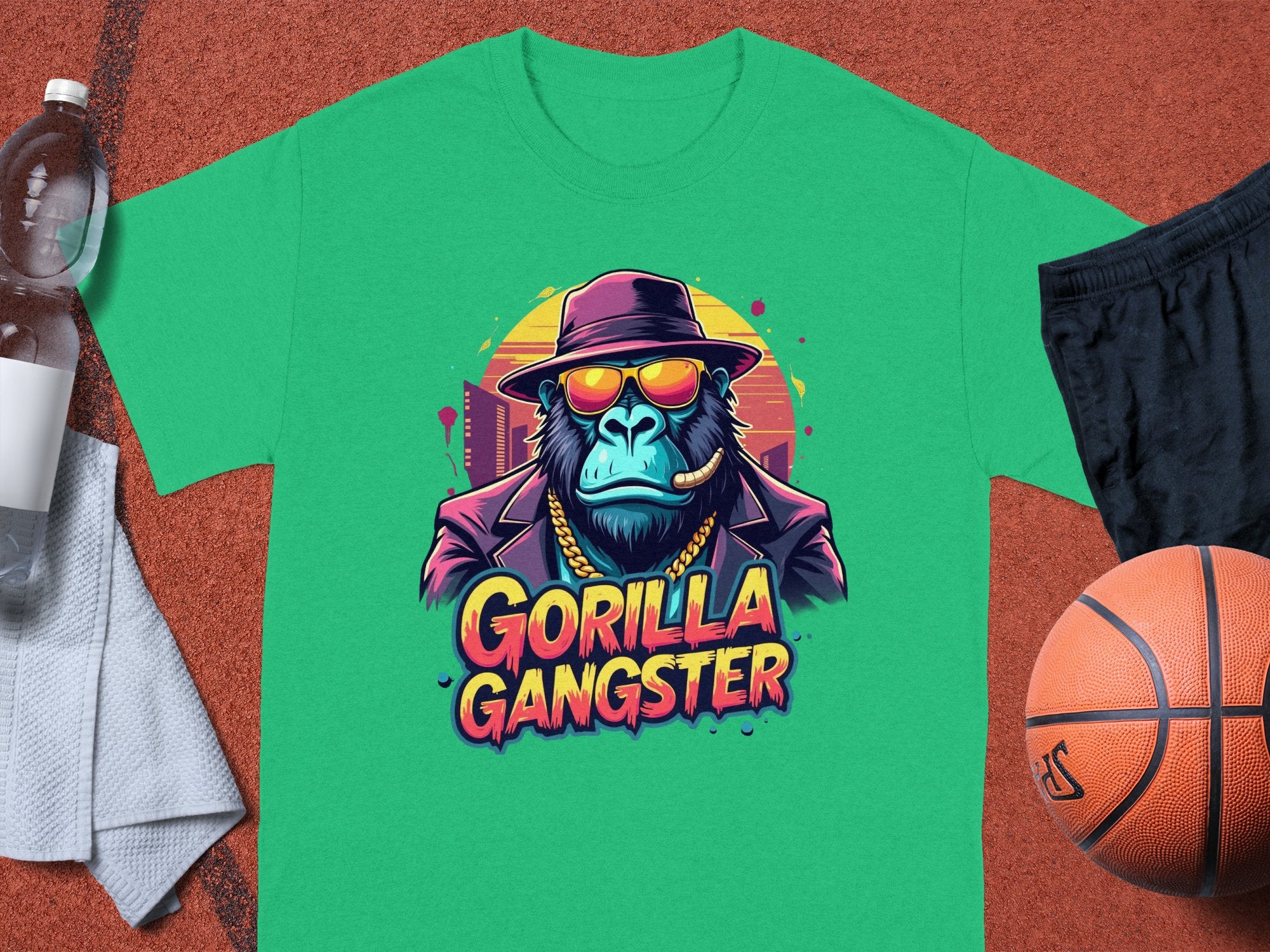 The Garment Graphics t-shirt boldly features a gorilla in a hat, sunglasses, and chain under Gorilla Gangster, set against an outdoor sports court backdrop with a basketball, towel, water bottle, and black shorts.