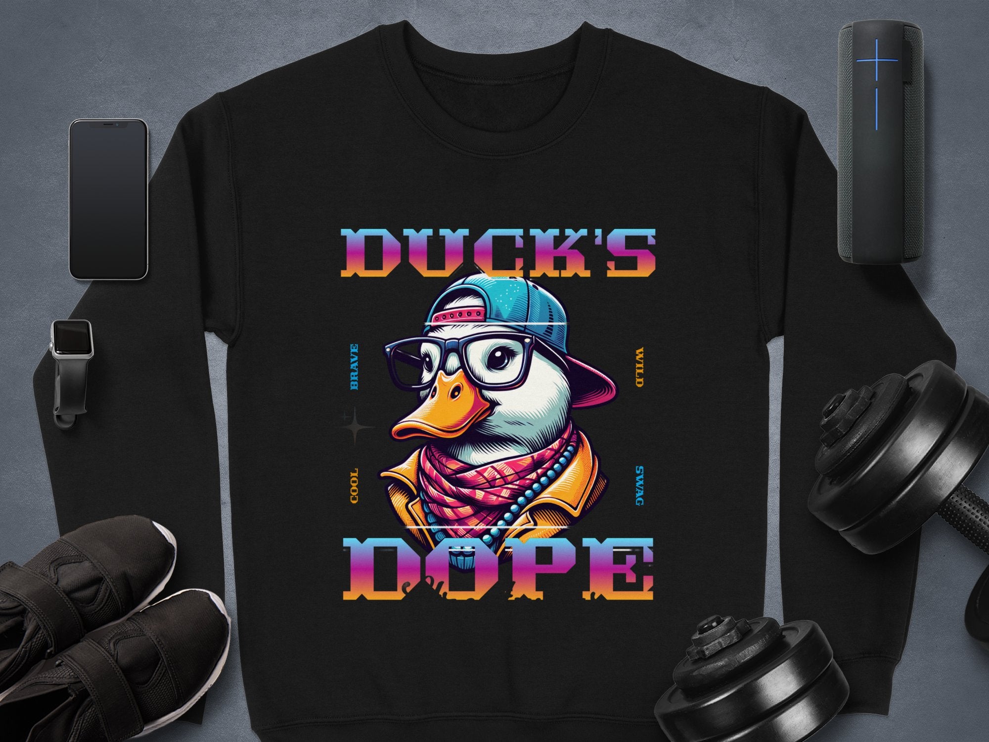 This black sweatshirt by Garment Graphics from the Brave Cool Swag Sweatshirts line features a duck wearing glasses, a cap, and a jacket. Ducks Dope is printed on medium-heavy fabric, displayed with a smartphone, smartwatch, sneakers, speaker, and dumbbells as an unisex piece.