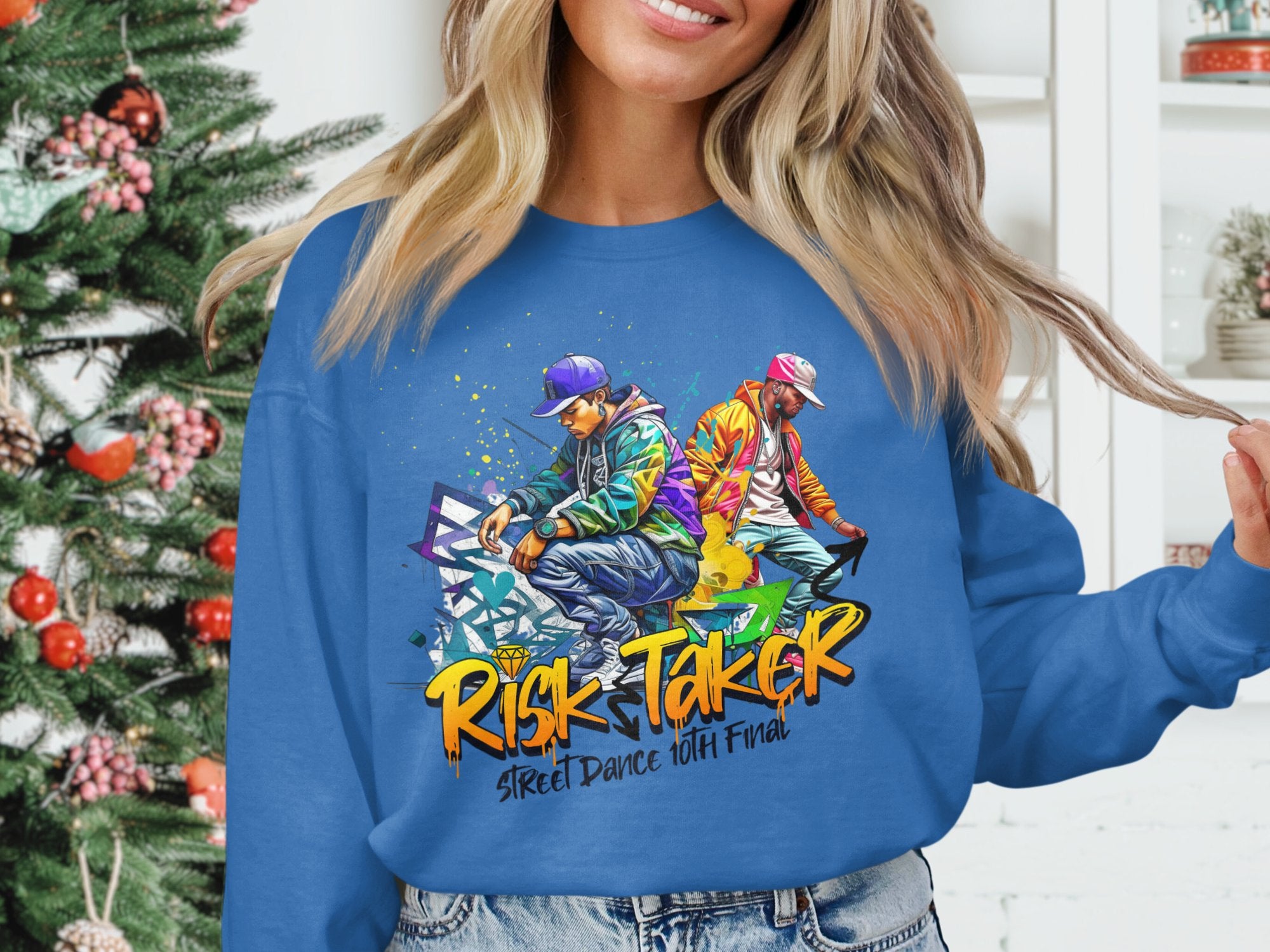 A person sports a Garment Graphics blue sweatshirt featuring two dancers in urban attire for the Risk Taker Street Dance 10th Final. A beautifully decorated Christmas tree in the background adds a festive touch.